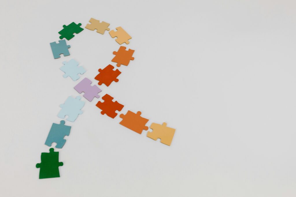 pexels-photo-8385962-8385962 Colorful puzzle pieces forming a ribbon shape on a white background, symbolizing awareness.